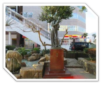 1階にコンビニが入っているビルを背景に、赤ちゃんを優しく抱く母親の姿を象ったブロンズ像が、赤い台座の上に立っている彫刻の写真