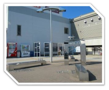 対曲線状に設置された4つの銀色に輝く金属製のベンチの中央に、門の様な形のコの字型のオブジェがあり、傍に空中に浮かんでいるようなヤジロベエの様な形をしたオブジェが特徴的な抽象的な彫刻が、駅前の広場に設置されている写真