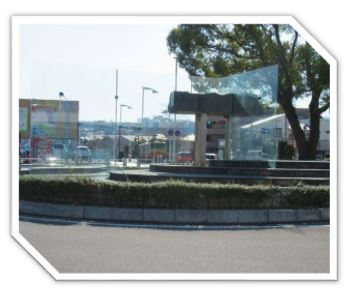 背景に一本の大きな木が立つロータリーの階段状の中央にガラス板がL字形で配置され、その間に鳥居の様な形をした重厚な黒御影石の物体が挟まれている抽象的な屋外彫刻の写真