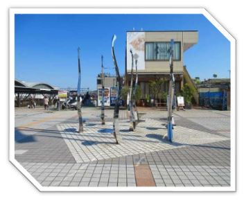 複数の光沢のある細長い金属製のポールが、不規則に地面から突き出ている抽象的な彫刻が広場に設置されている写真