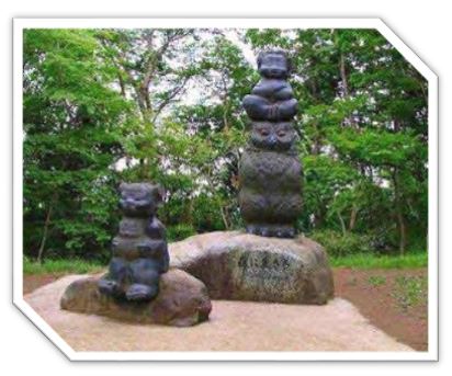 緑豊かな木々を背景に、前後に並んだ不揃いな石の土台の上に、頭の上に腕を組んだ猿が乗った大きなフクロウ、もう一つの石の上にクマのような動物が座っている様子を表現した屋外彫刻の写真