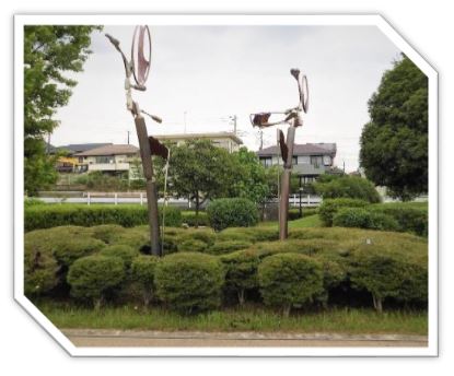 密集した小さな植え込みの中に、2本のステンレス製の棒の上に、円形の金属片が溶接された、一対の奇妙な形状をした抽象的な現代彫刻の写真