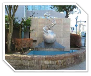 3人の人物が手を取り合い、丸い地球儀のような物体の上で弧を描くように連なっている、金属製の抽象的な屋外彫刻の写真