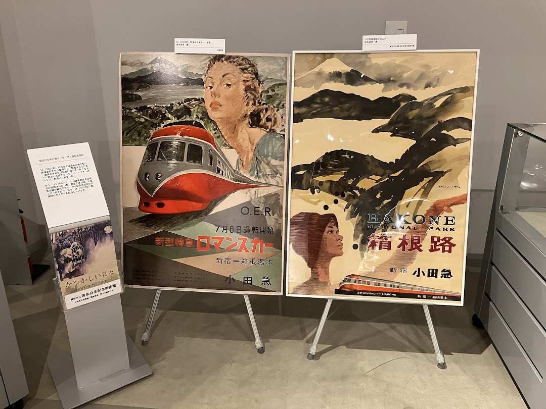 左側に説明版が設置され、左に「新型特急ロマンスカー」と書かれたポスターが、右に「HAKONE NATIONAL PARK 箱根路」と書かれた2枚のポスターが展示されている写真