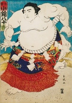 上半身裸の力士が、白いまわしと赤や青色が入った化粧まわしを身につけて、両手と両足を大きく広げて土俵上に立つ初代小錦八十吉の姿を描いた、歌川国芳による迫力ある相撲絵の浮世絵