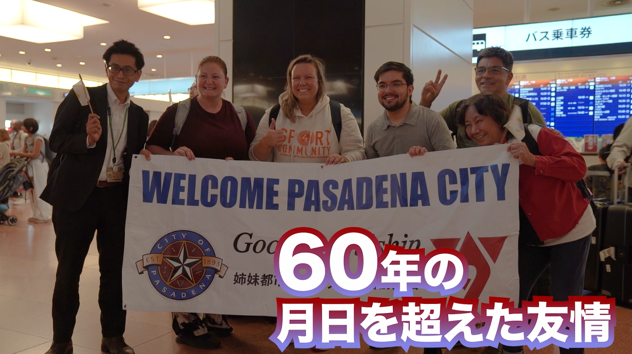 「60年の月日を超えた友情」という文字が大きく表示され、駅の改札でスーツ姿の日本人男性と5人の外国人の方々が、「WELCOME PASADENA CITY」と書かれた横断幕を持って笑顔で並んでいる姉妹都市交流の記念写真
