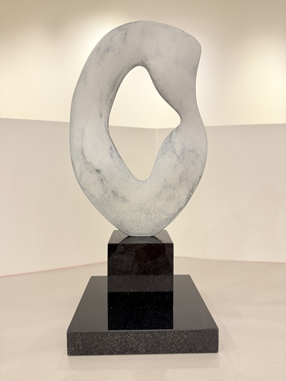 黒い台座の上に、白とグレーの斑模様の中央に孔が空き、帆をイメージした形で、滑らかな曲線を持つ抽象的な彫刻の佳作受賞作品の写真