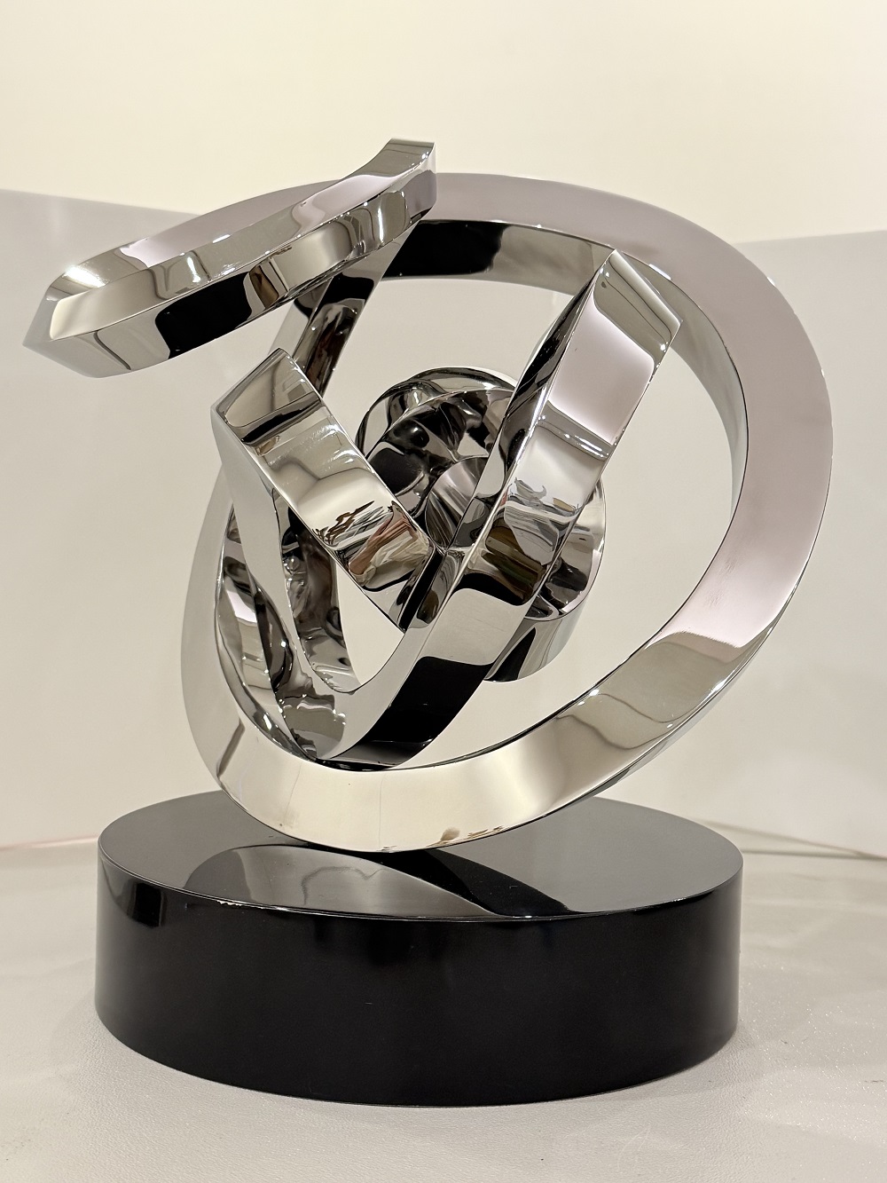 円形の黒い台座の上に置かれた、つややかな鏡面仕上げの金属で、大きな円の中に小さな円が重なった複数の円や角ばった面が複雑に絡み合い、抽象的な形状の現代彫刻の佳作受賞作品の写真