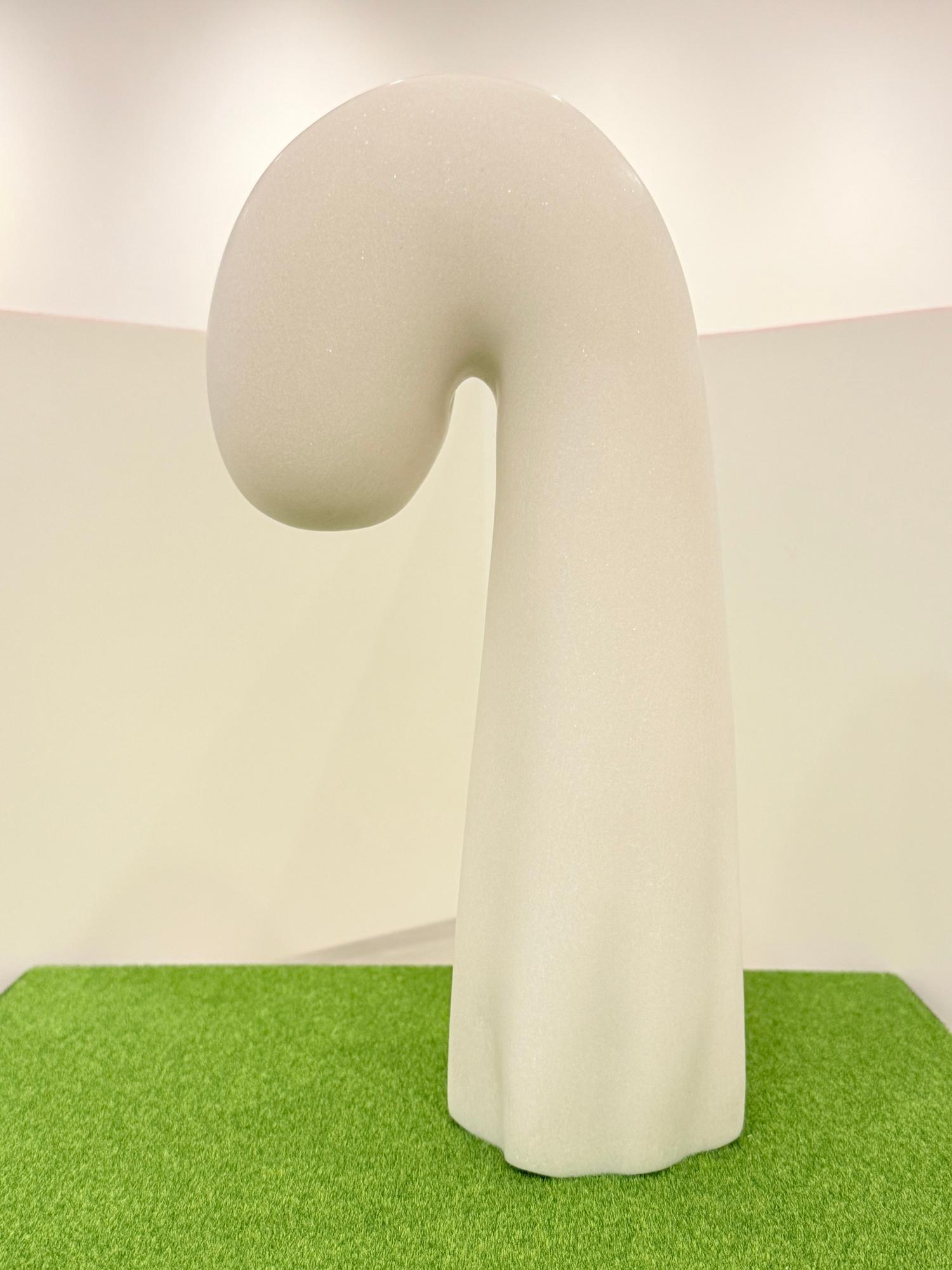 芝生の上に立つ、白く滑らかな質感が特徴的な、曲線を描いて上部が垂れ下がった、杖やフックのような形をした抽象彫刻の佳作受賞作品の写真