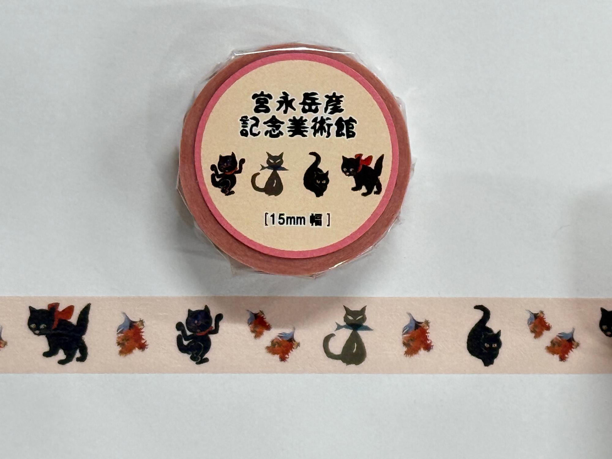 サーモンピンク色の台紙に「宮永岳彦記念美術館」の文字と四匹の黒猫が描かれたマスキングテープのパッケージと、その下に、黒猫や葉っぱのようなモチーフが繰り返し印刷されたマスキングテープが広げられた状態の商品写真
