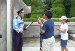 制服姿の男性が持った長い棒の先についた火を、3人の訪問団員の子供たちが持つロウソクに採火している様子の写真