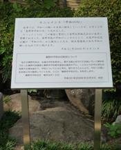 緑の木々に囲まれて立っている、銀色のポールに固定された秦野市平和の日の内容が記されている白い説明板の写真