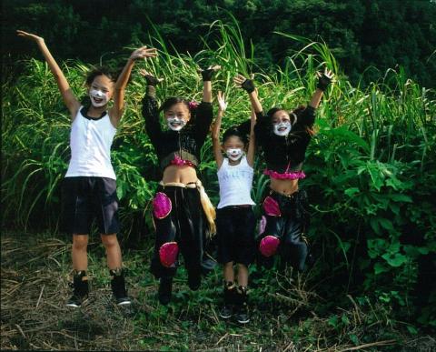 緑豊かな草木を背景に、口回りに白のペイントを施した、満面の笑みを浮かべた4人の子どもたちが、横一列に並んで両手を広げてジャンプしている、躍動感あふれる写真の部で市展大賞を受賞した作品の写真