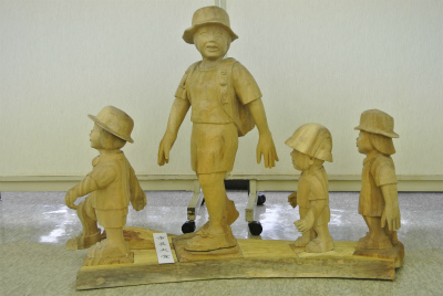 通学帽とランドセルを背負った子どもたちの姿が、大きな子どもを先頭に連なって歩いている様子を木彫りで立体的に表現した、美術の部で市展大賞を受賞した作品の写真