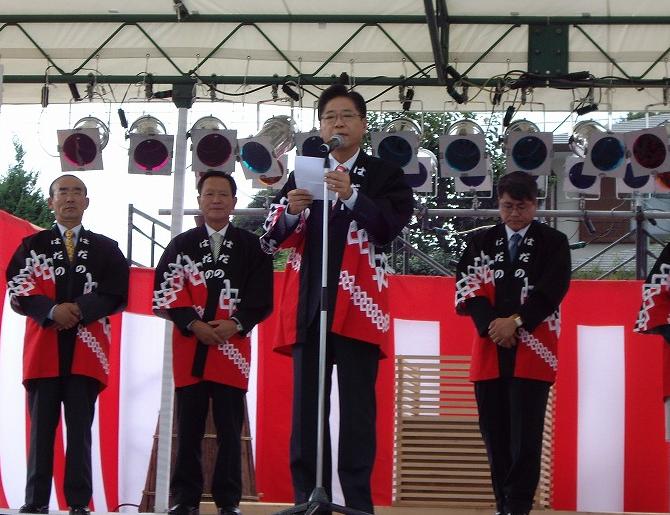 特設ステージの上で、赤と黒の法被を着用した複数の男性が並んでおり、中央に立つ眼鏡をかけた柳坡州市長がマイクに向かい、紙を見ながら挨拶をしている式典の写真