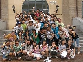 階段状の建物の入り口前で、大勢の男女が様々なポーズをとり、中には数名の外国の学生も含まれており一緒に記念撮影をしている様子の写真