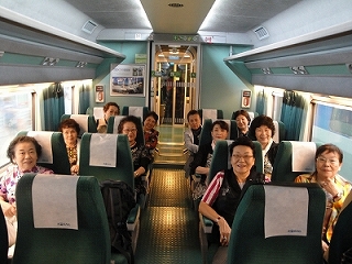 韓国の特急列車と思われる緑色の座席が並ぶ車両内で、訪問団の一団を構成する多くの年配の女性たちが、旅行を楽しみながら乗車している様子を捉えた写真