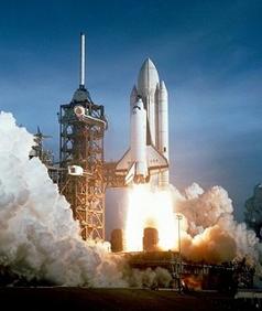 濃い青空の下、スペースシャトルが発射台から巨大な炎と大量の白煙を噴き出しながら垂直に上昇し始めている、力強い打ち上げの瞬間を捉えたNASAの写真