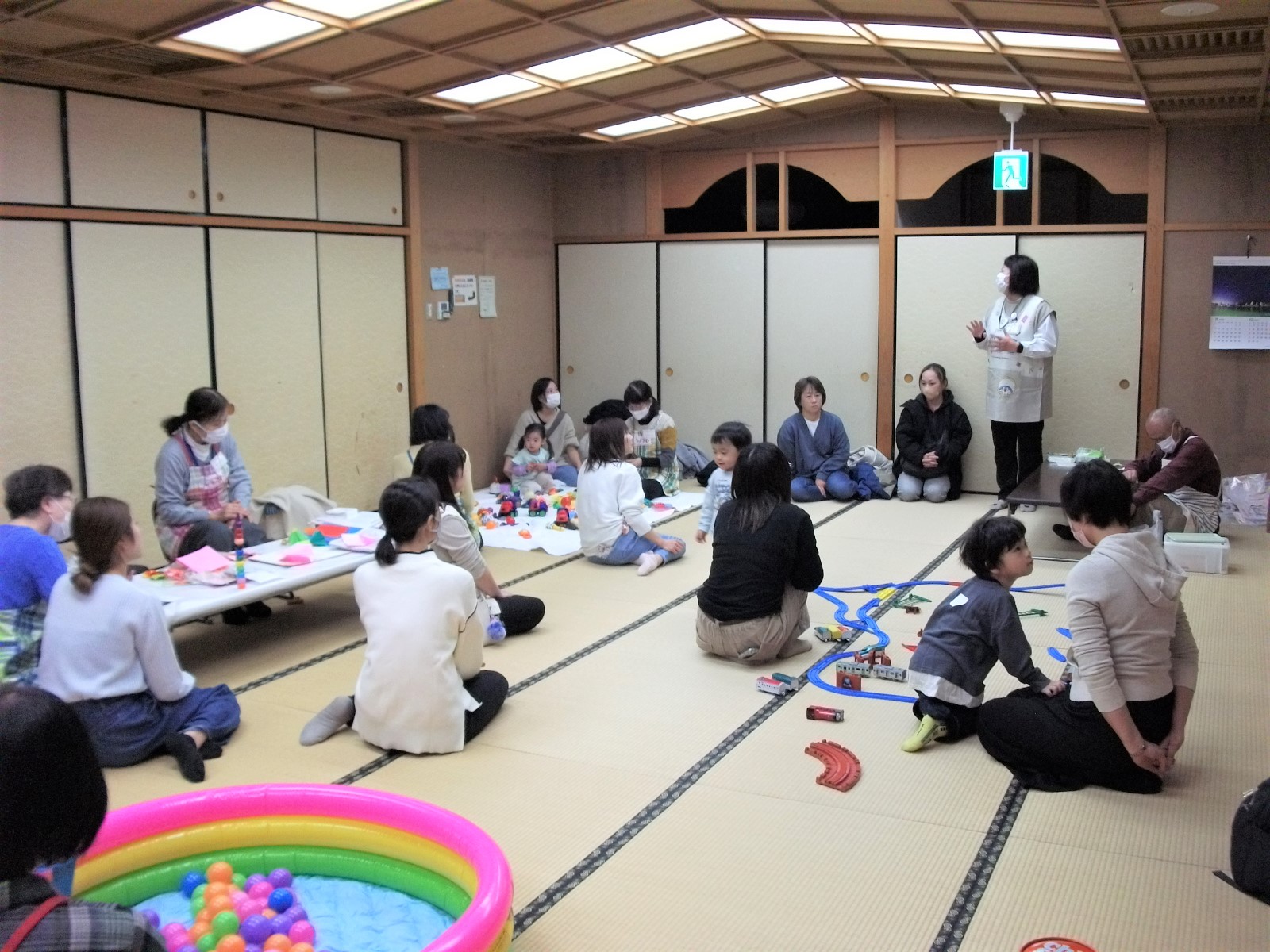 畳の部屋で、複数の子どもと大人がテーブルを囲みながら紙工作や遊びを楽しんでいる様子を写したひよこサロンの写真