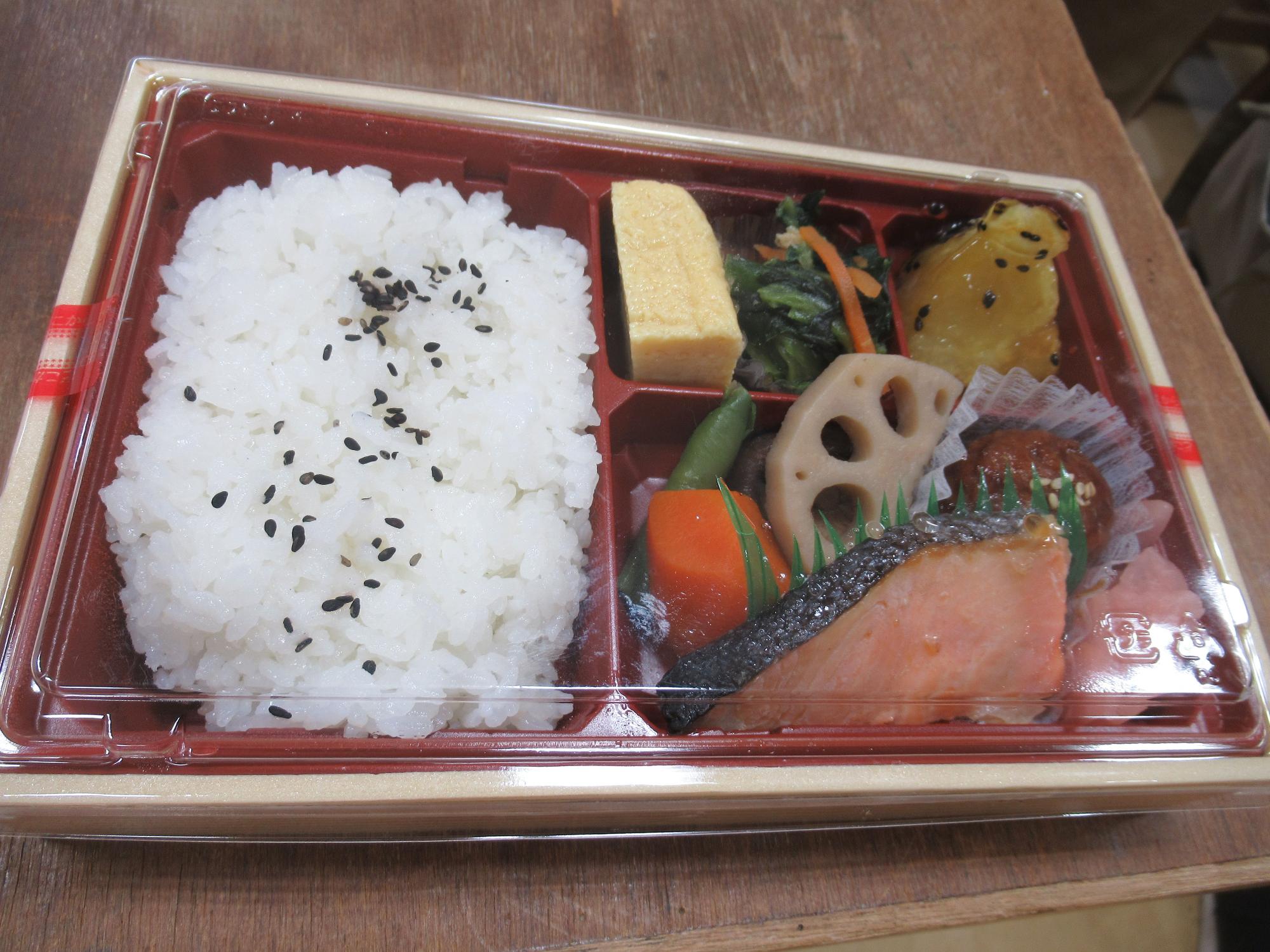 黒ごまがかかったご飯と、焼き鮭、卵焼き、煮物、酢の物などが彩りよく詰められている、バランスの取れた和食の弁当を真上から撮影した写真