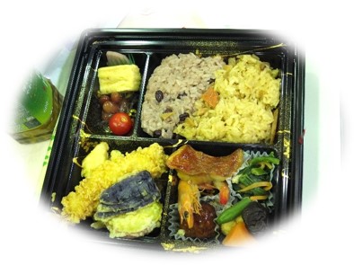 黒いプラスチック製の容器に、お赤飯と黄色の炊き込みご飯、海老の天ぷらと野菜の天ぷら、煮物、卵焼き、ミニトマトなどが彩りよく詰め合わされた弁当の写真