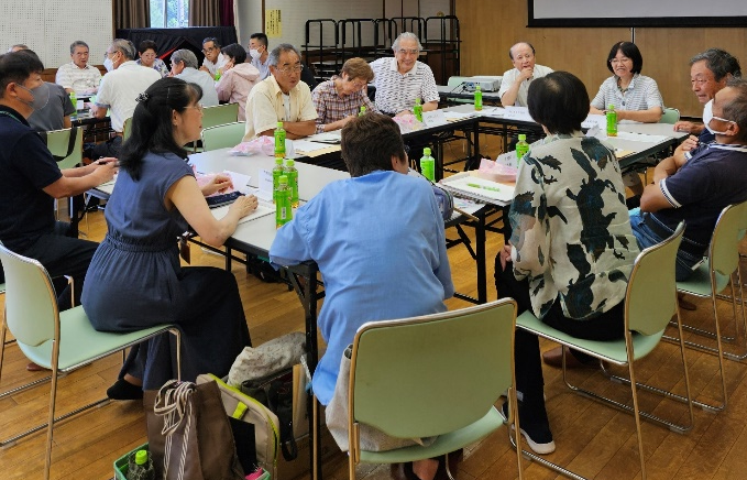 会議室で、大勢の参加者が複数のテーブルに分かれて座り、活発に話し合っている様子の写真