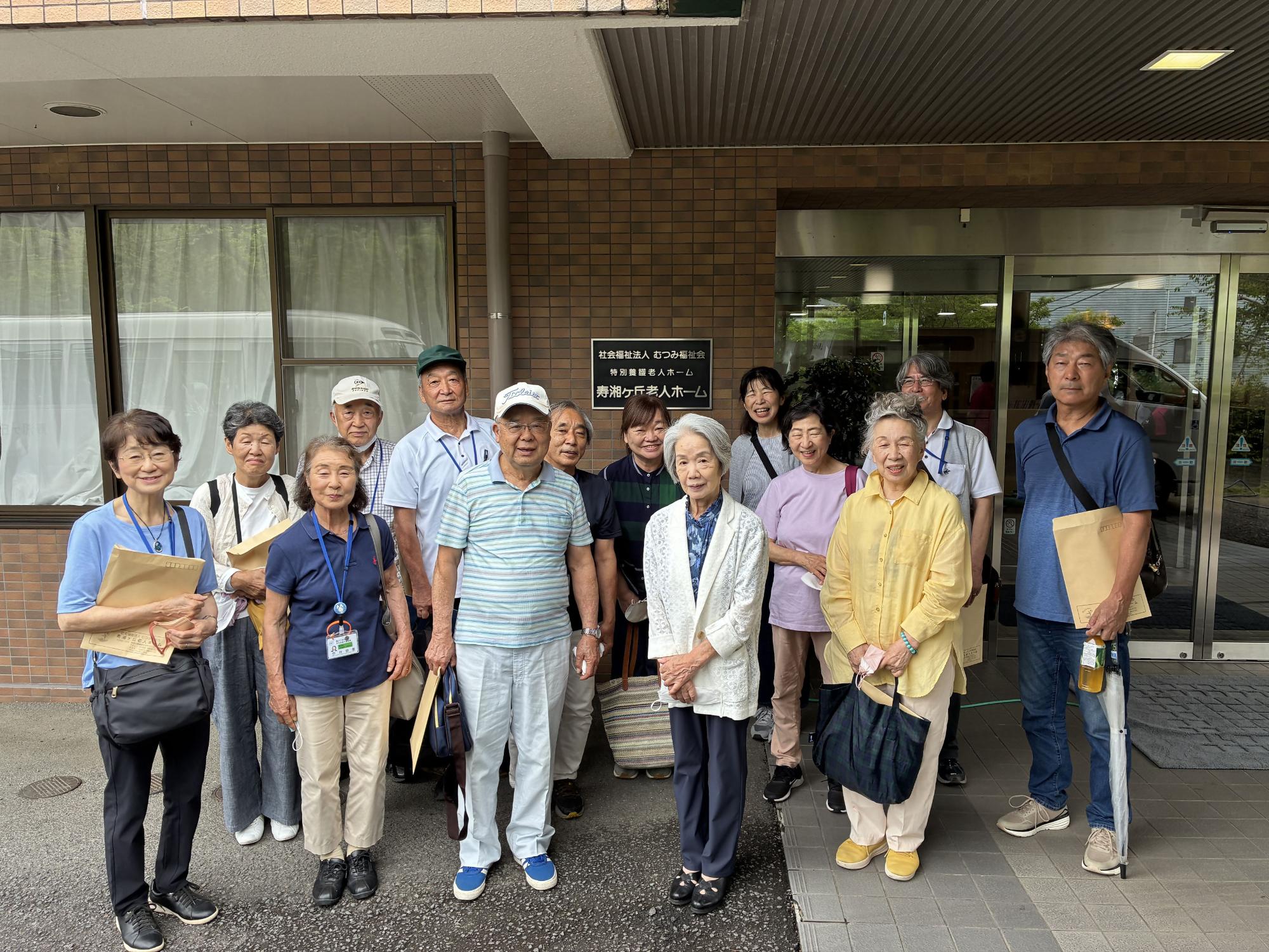 施設や建物の入り口前で、複数の高齢者がにこやかに並んでいる集合写真