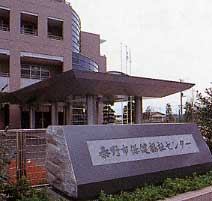 ベージュ色の外壁の建物が建っている入り口に、「秦野市保健福祉センター」と書かれた石の看板が設置された写真