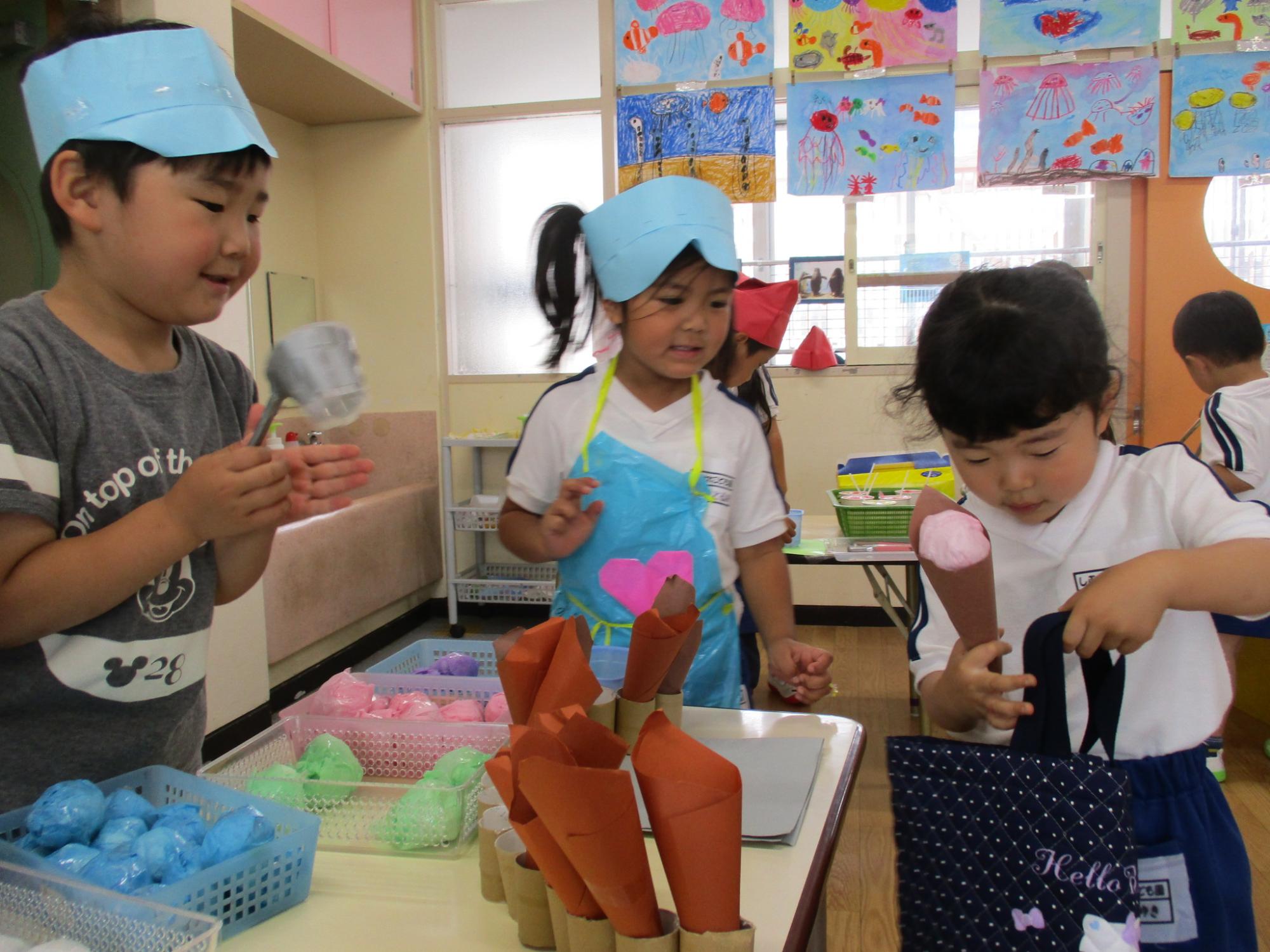 折り紙や紙コップを使って作ったアイスクリームやコーンで子供たちが店員やお客さんになり遊んでいる様子の写真