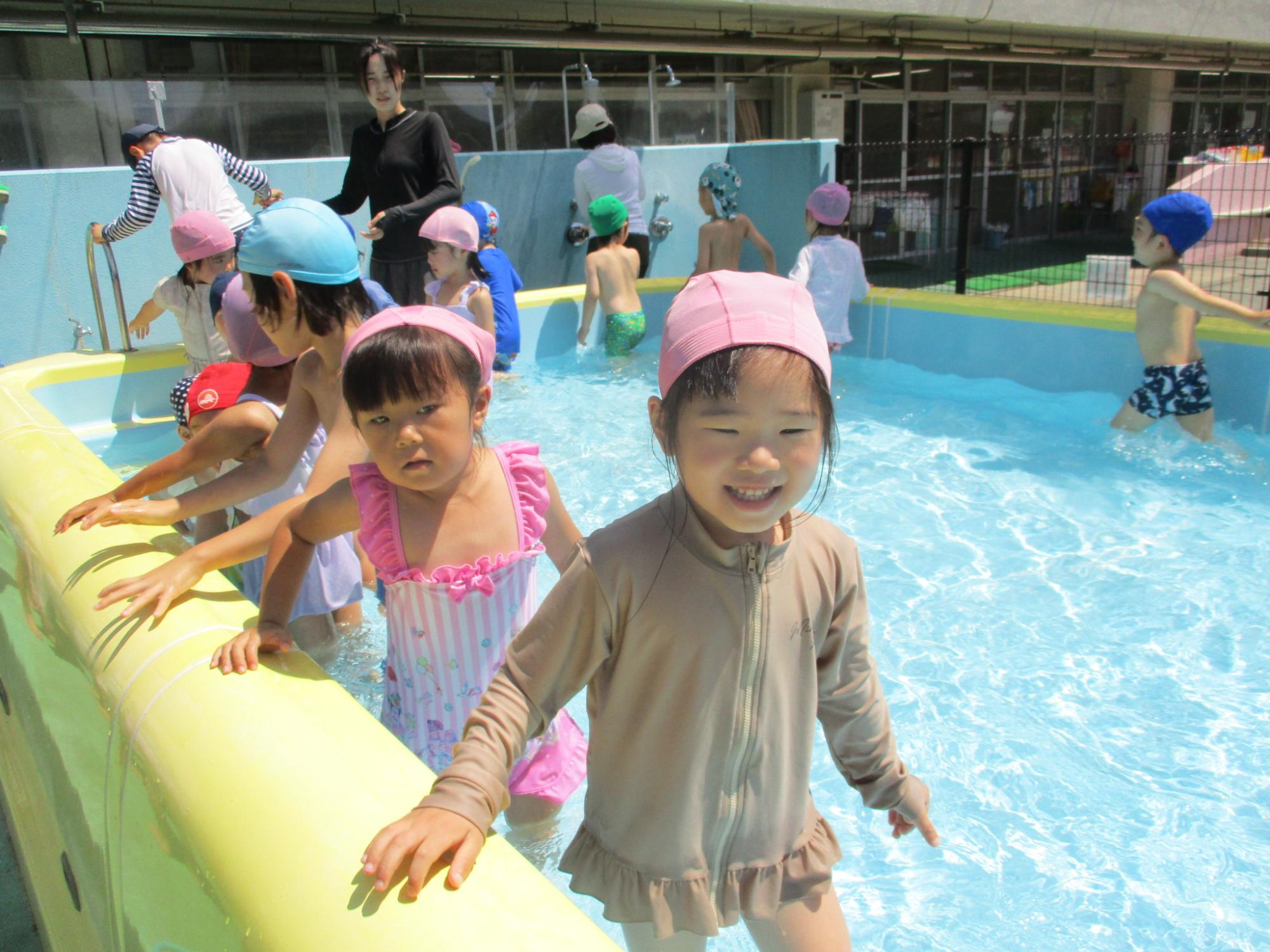 たくさんの子供たちが、先生に見守られながら、笑顔でプール遊びを楽しんでいる写真