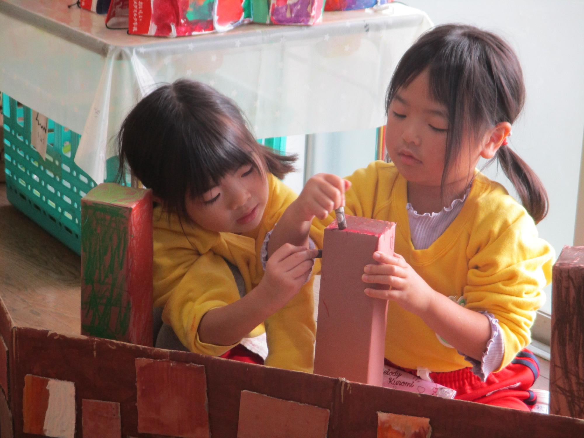 2人の園児が、ダンボールでできた工作物を熱心に色塗りをしている様子の写真