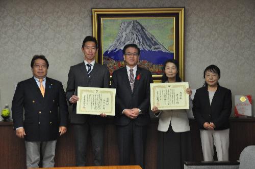 金色の額縁に入った山頂に雪が積もった大きな山の絵画を背景に、笑顔の市長を中央に保育賞を受賞した2人が賞状を持って立ち、2人の関係者と共に横一列に並んでいる令和5年度表彰式の写真