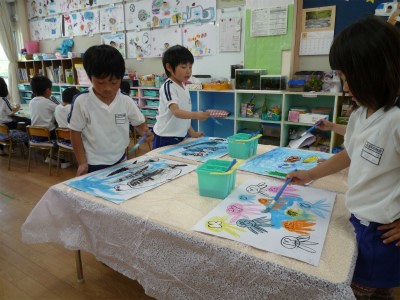 子供たち2人ずつ向かい合って、立ちながら絵具を使って絵を描いている様子の写真