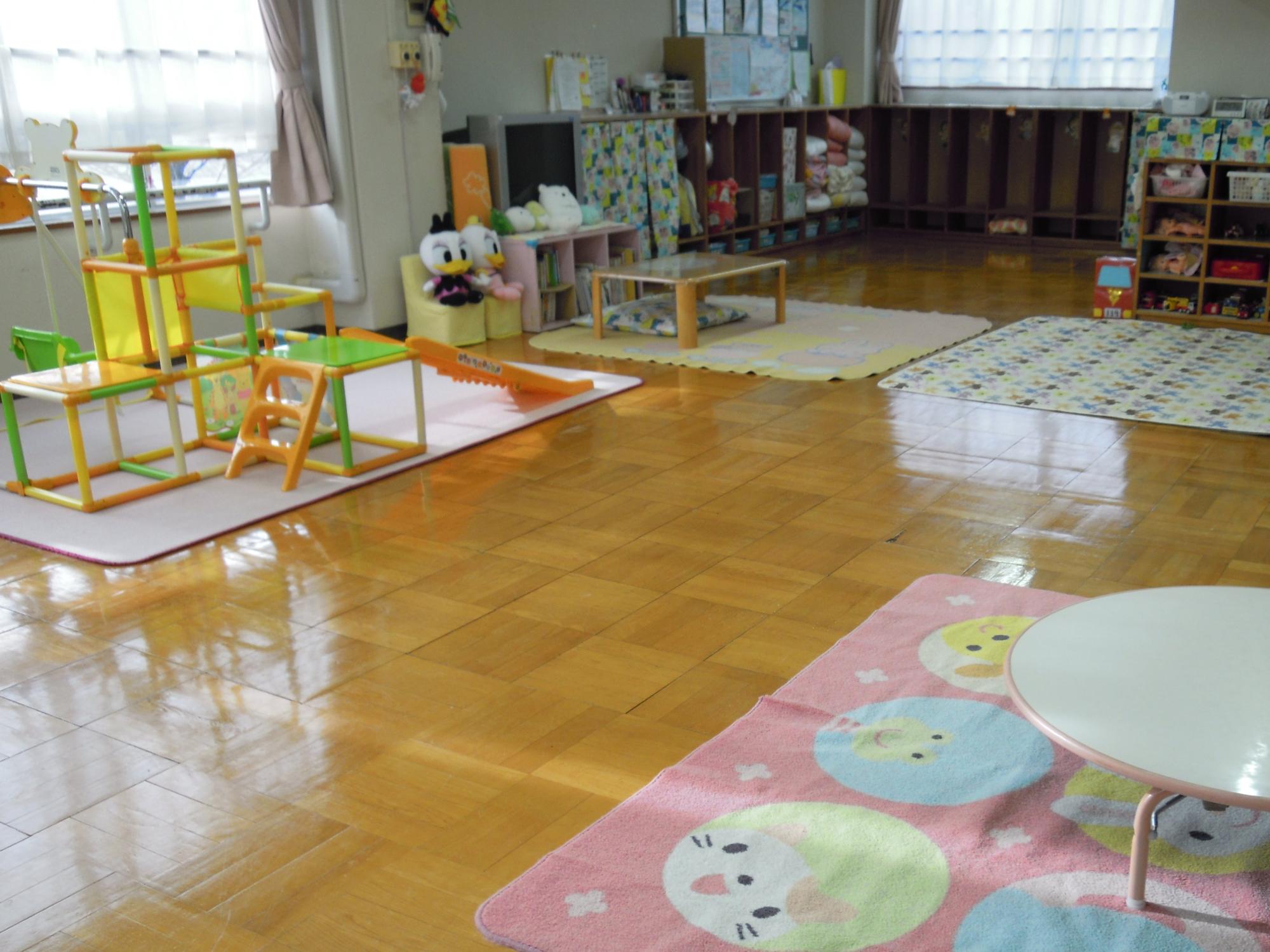 絨毯の上に室内用のジャングルジムがあり、子ども用の椅子の上にはアヒルのキャラクターの人形が座っているくまサンルームの写真