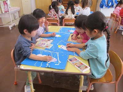 3歳児の園児たちが画用紙にクレパスを使って、友達と笑いながら雪だるまの絵を描いている様子の写真