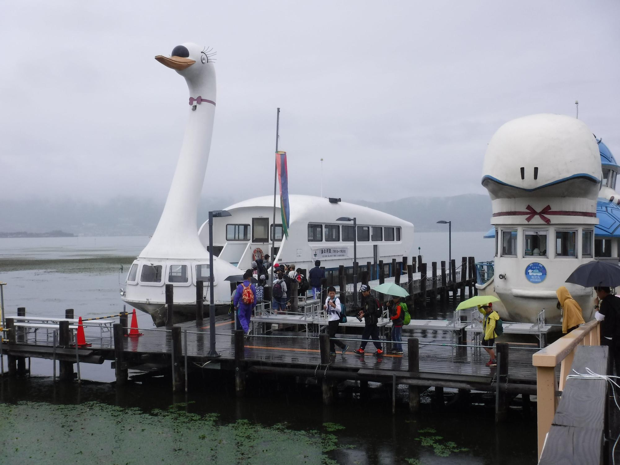 白鳥の遊覧船が停泊しており、子供達や大人が桟橋を渡って遊覧船に乗車している写真