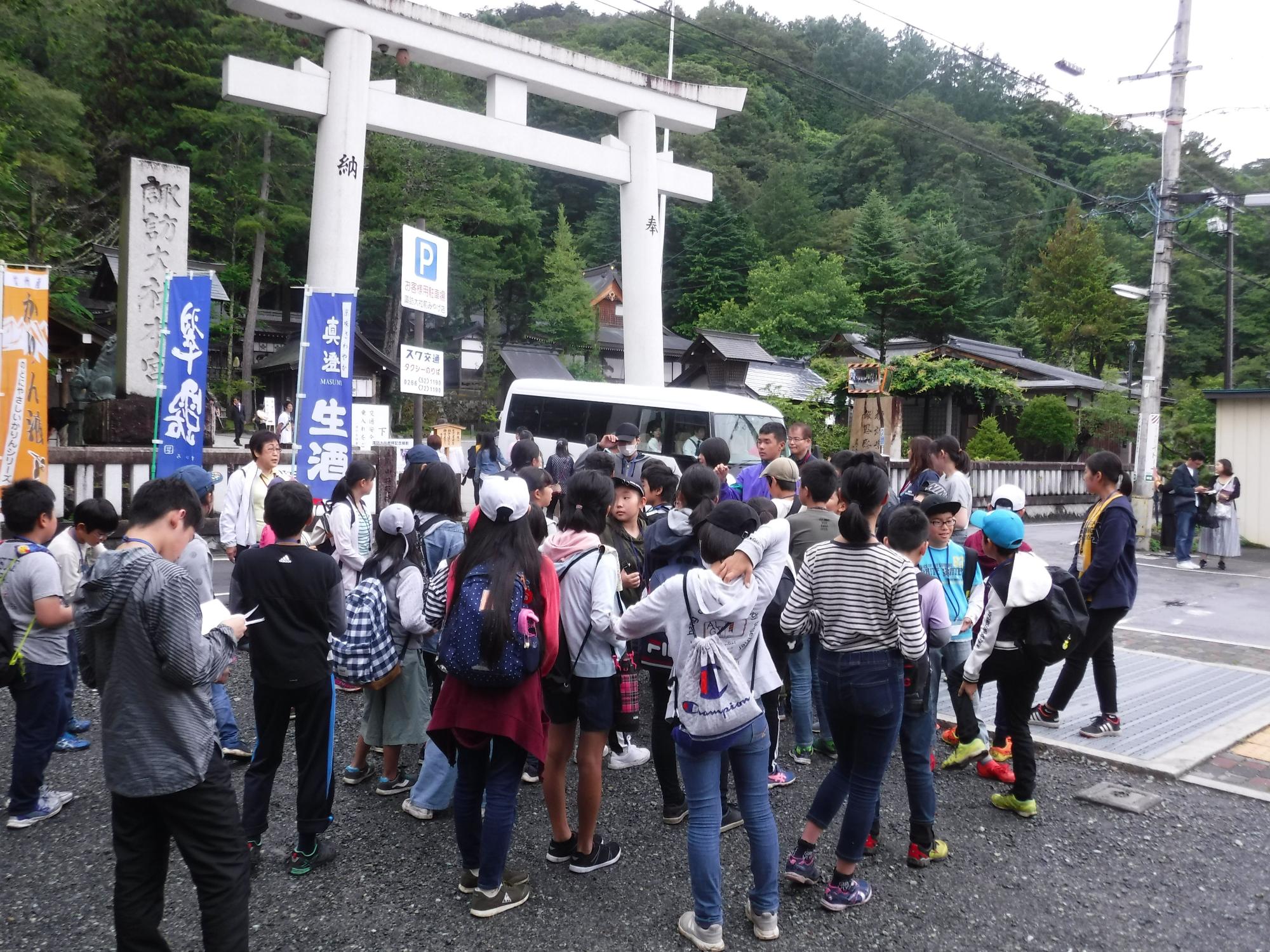 木々に囲まれた鳥居前で、子供達や大人が集合している写真