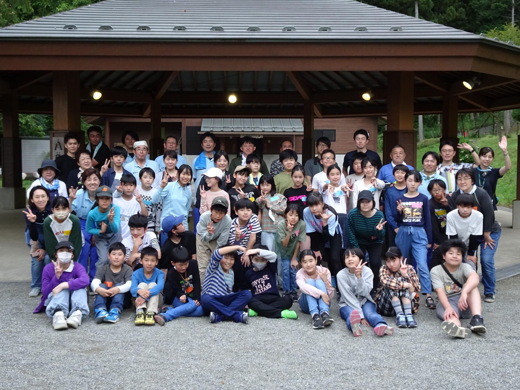 施設前で、参加した複数の子供達や大人が笑顔でポーズをとっている集合写真
