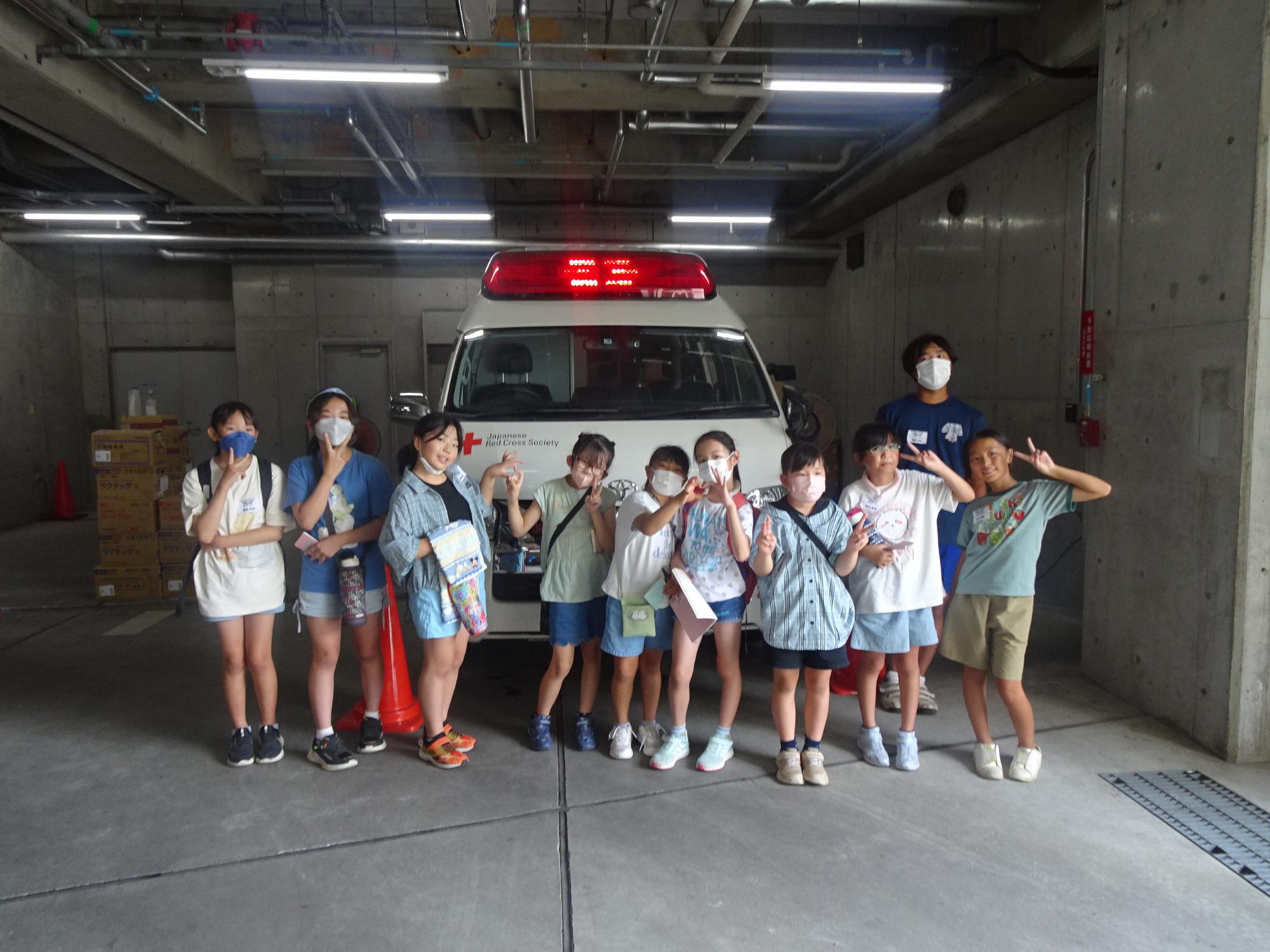 緊急車両の前で、マスクをつけた子供達がピースサインやポーズをとっている写真