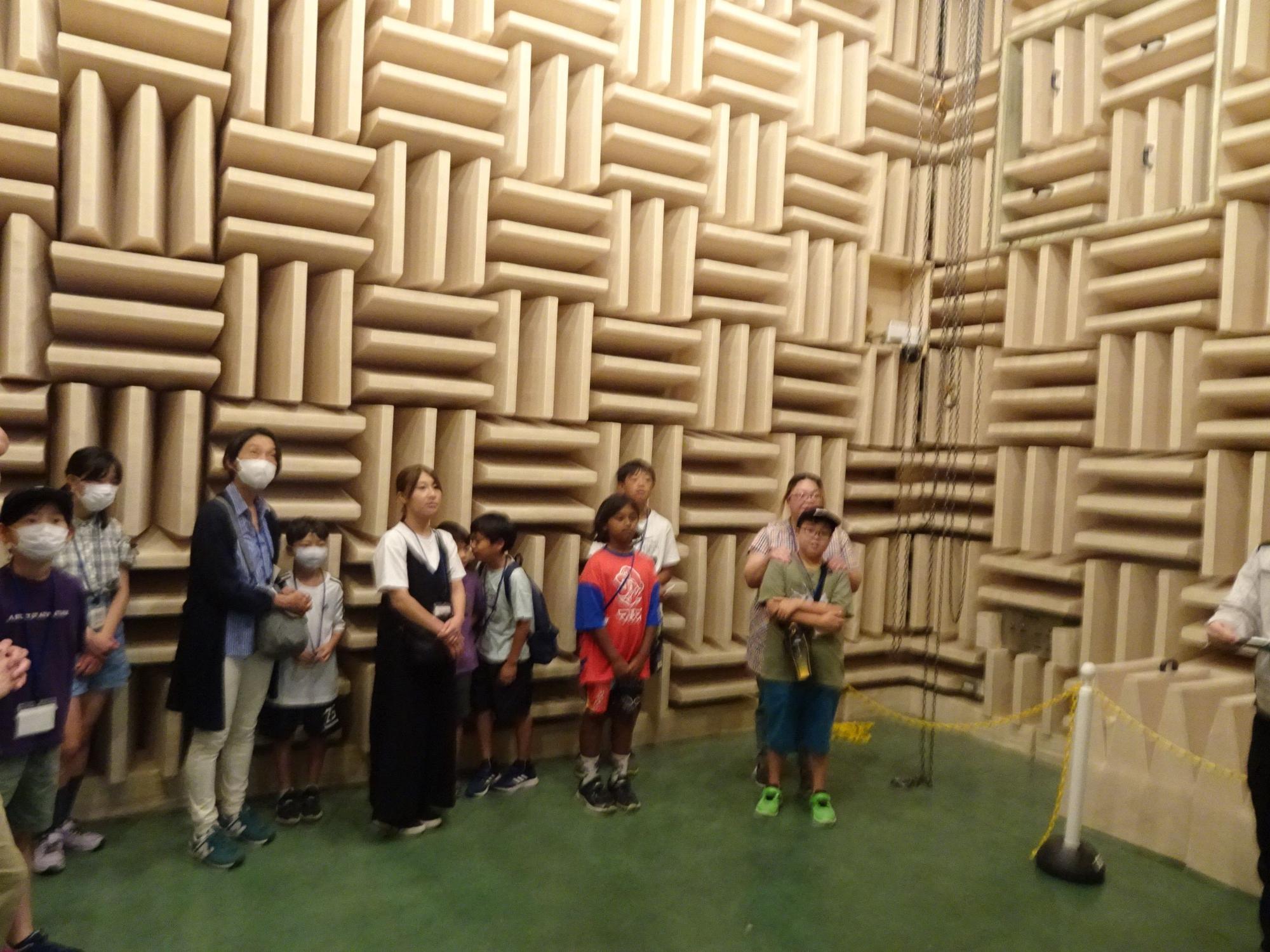部屋全体が音を吸収する吸音材で覆われた無響室で、説明を聞く大人と子供達の写真
