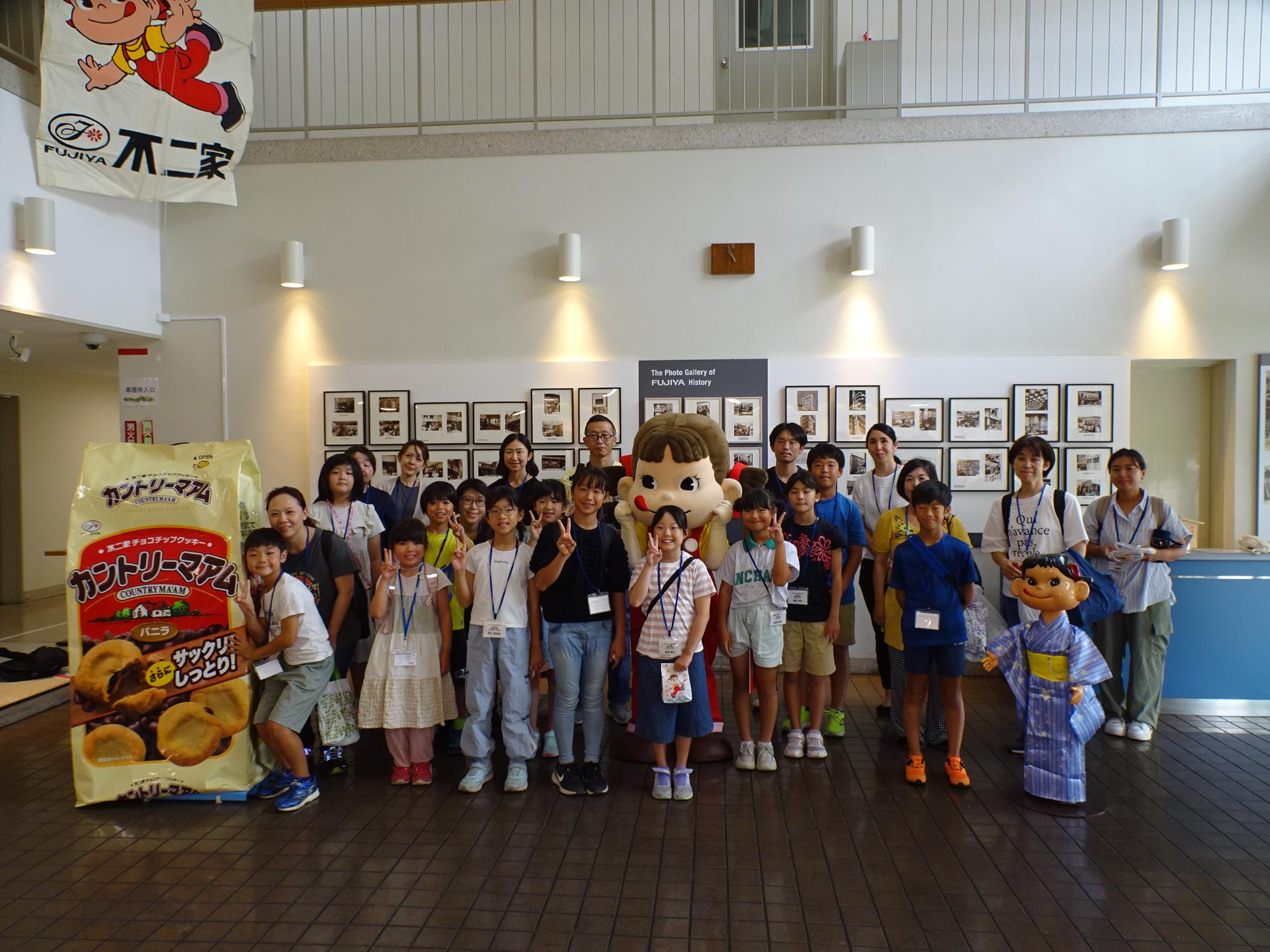 赤いリボンを付けて口をペロっとした大きなマスコット人形や、大人の背丈ほどある巨大なカントリーマアムの袋の横に、参加した複数の大人や子供達が笑顔で集合している写真