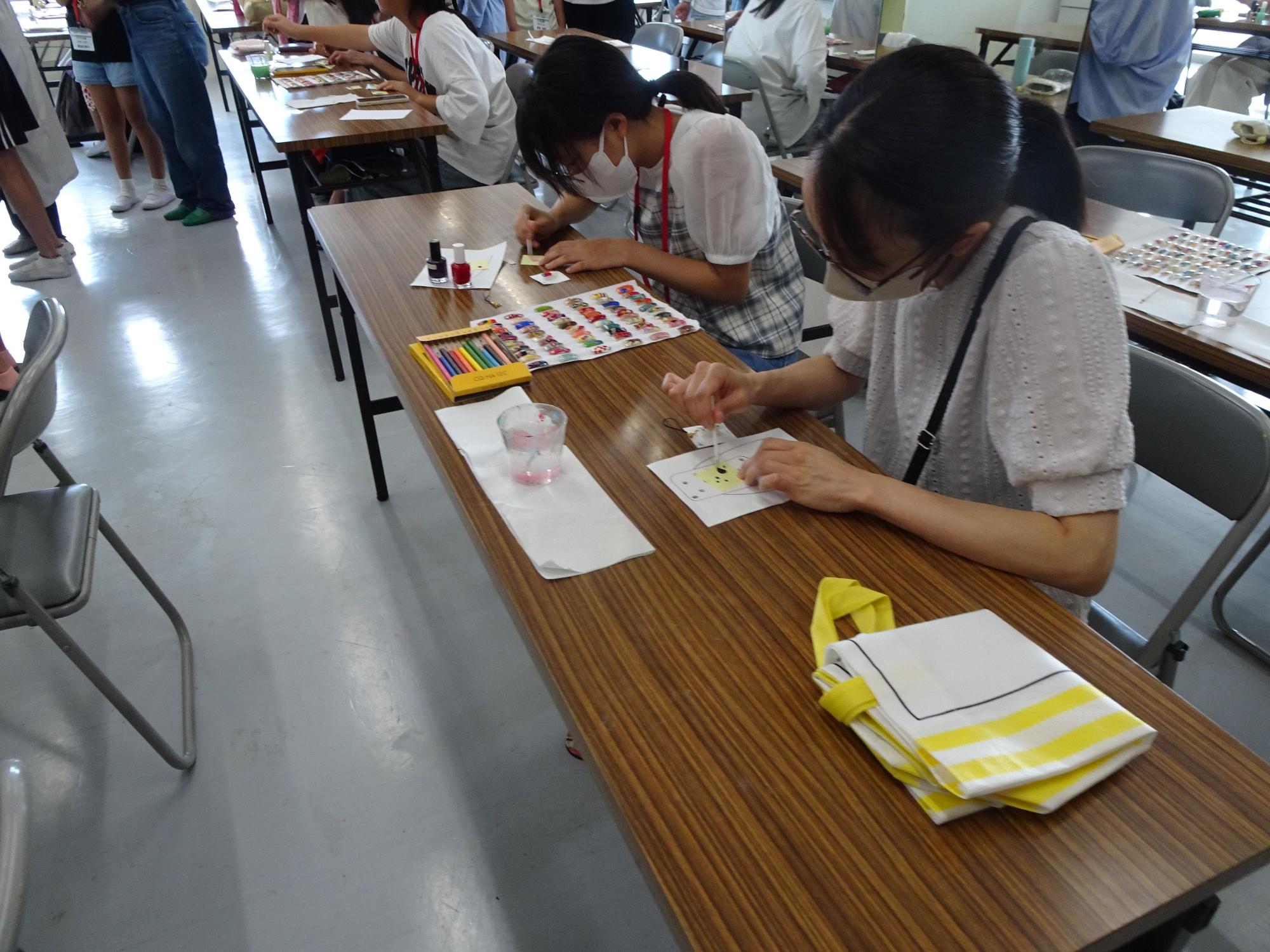 長机に小中学生が席に座り、色鉛筆や筆を使いネイルチップにイラストを描いている写真
