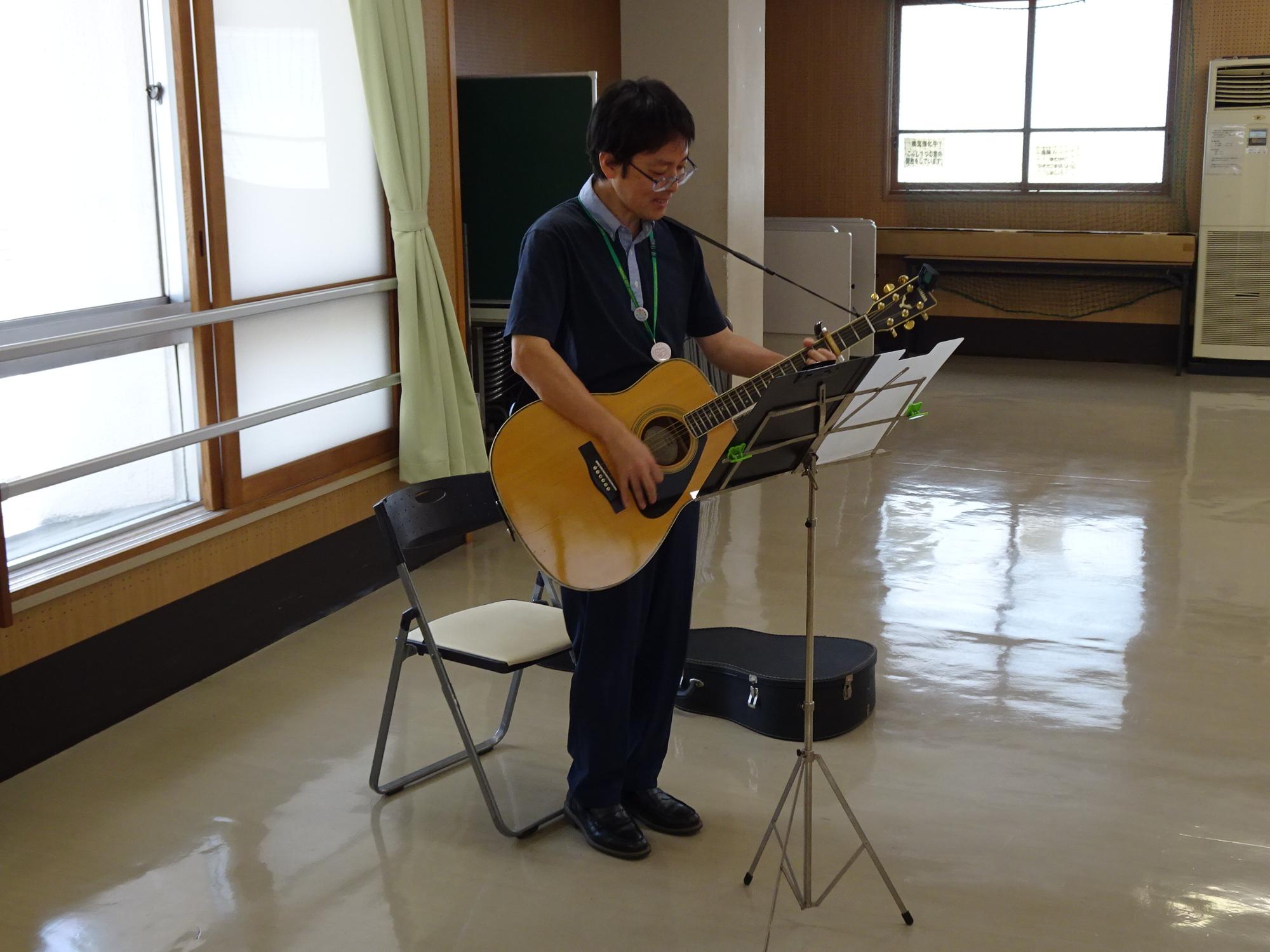 男性が立ってアコースティックギター弾いている写真