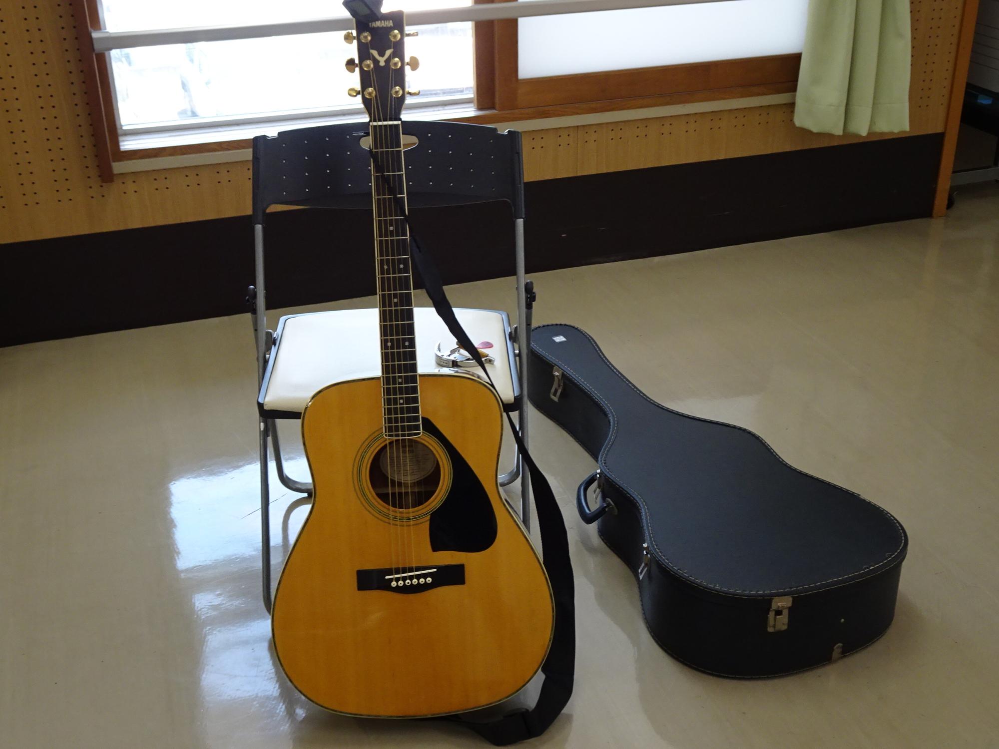 アコースティックギターが椅子に立てかけられており、その隣にはギターケースが置かれている写真