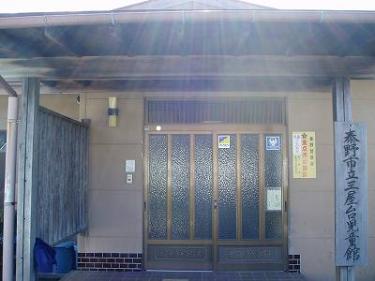 薄茶色の壁と焦げ茶色の屋根の建物で、玄関には金色の枠の入った曇りガラスのドアがあり、右の壁には「秦野市立三屋児童館」と書かれた木製の看板が立てられている三屋台児童館外観写真