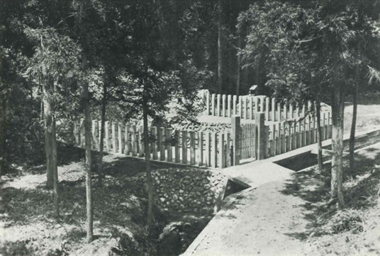 鬱蒼とした木々に囲まれた中に、石積みの土台の上に木製の柵と扉が建てられ、その柵で囲まれた中央部分の奥には祠のような小さな構造物が見える、大正時代の紀伊ノ守の水源を写した白黒写真