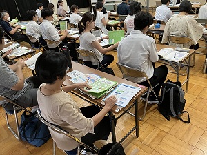 教室で複数の人が机に向かって座り、配布された資料を見ながら講師の話を聞いている様子を写した、指導者養成講座の写真