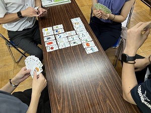 テーブルの上に並べられたカードゲームを複数人がプレイしている様子の手元を写した、交流型ゲーム活動の写真