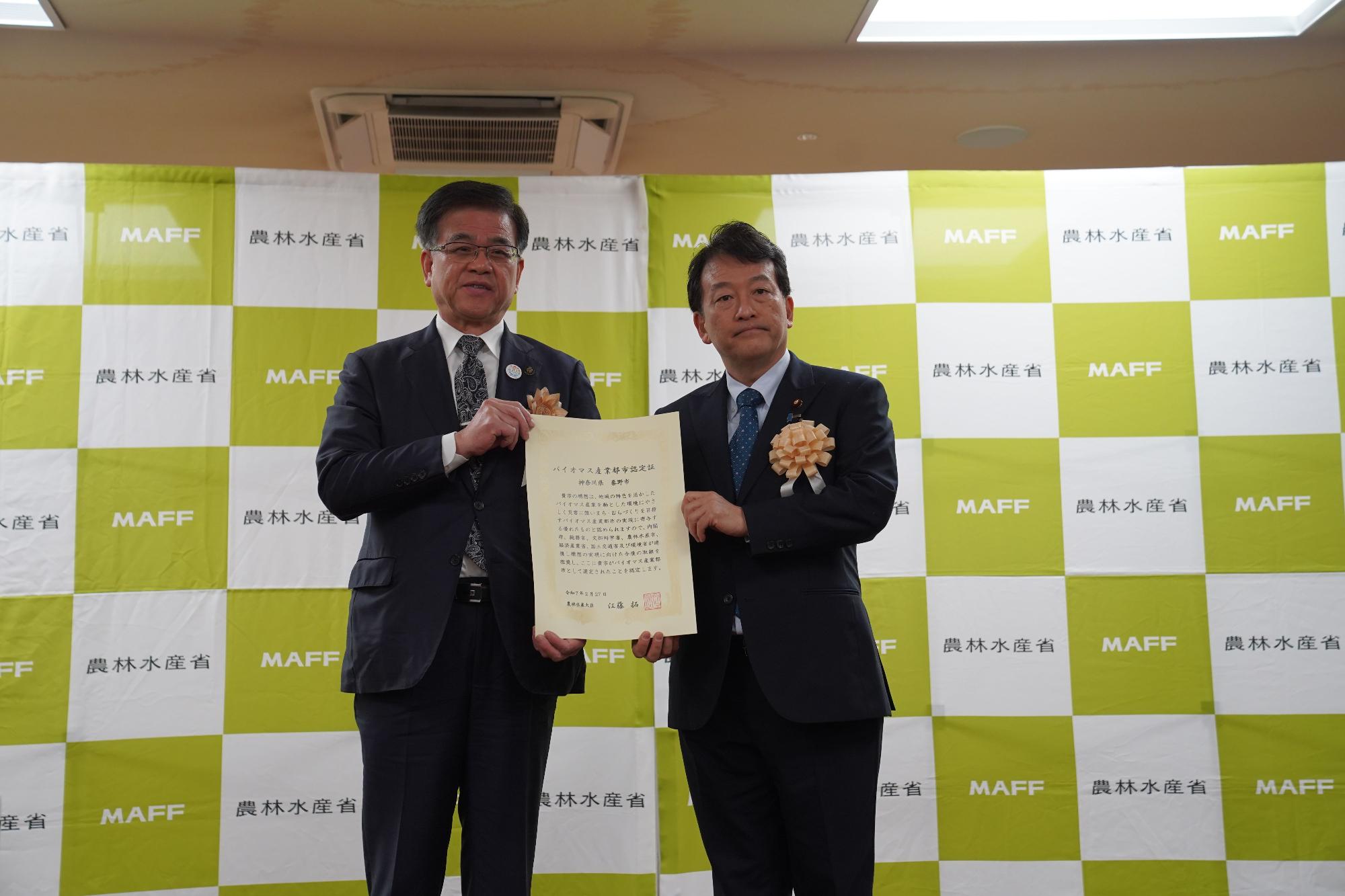 農林水産省のバックパネルの前で、笹川農林水産省副大臣と市長が一緒に賞状を持て並んでいる写真