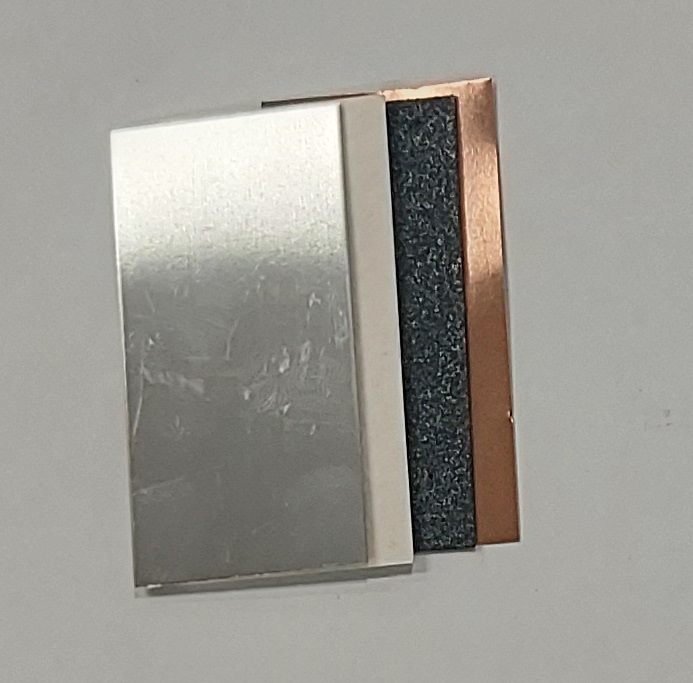 表面に細かい擦り傷のある光沢のある銀色のマグネシウム板が一番手前にあり、その後ろから、白い層のセパレーター紙、ざらざらした黒い層のカーボン板、そして赤銅色の銅板の計4層の板状の素材が少しずつずれて重なっているクローズアップ写真